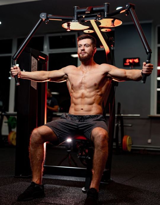 An athletic man doing doing machine chest fly exercises at the gym.