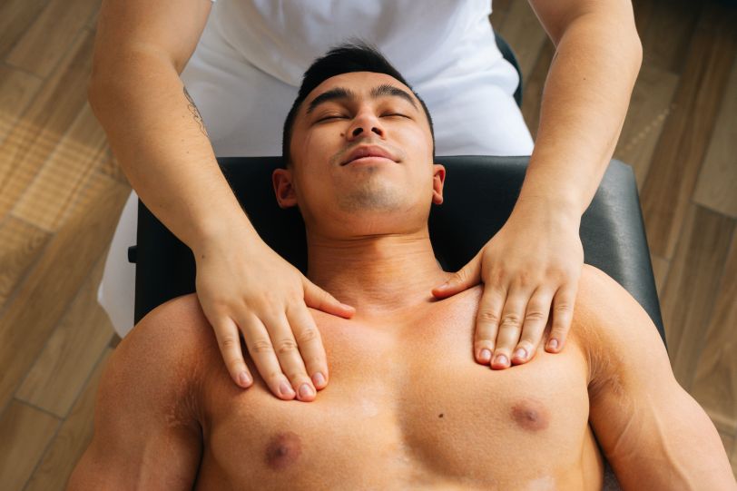 Un terapeuta de masajes realizando masaje de drenaje linfático en el pecho de un hombre después de la cirugía de ginecomastia.