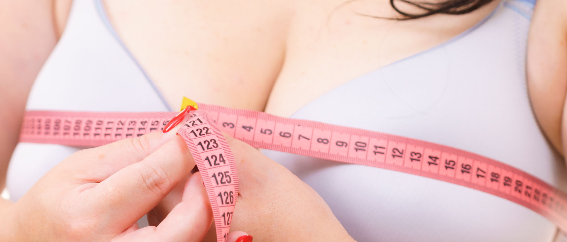 Closeup of female breasts, woman wearing bra using tape measure to check the measurements of her big chest.