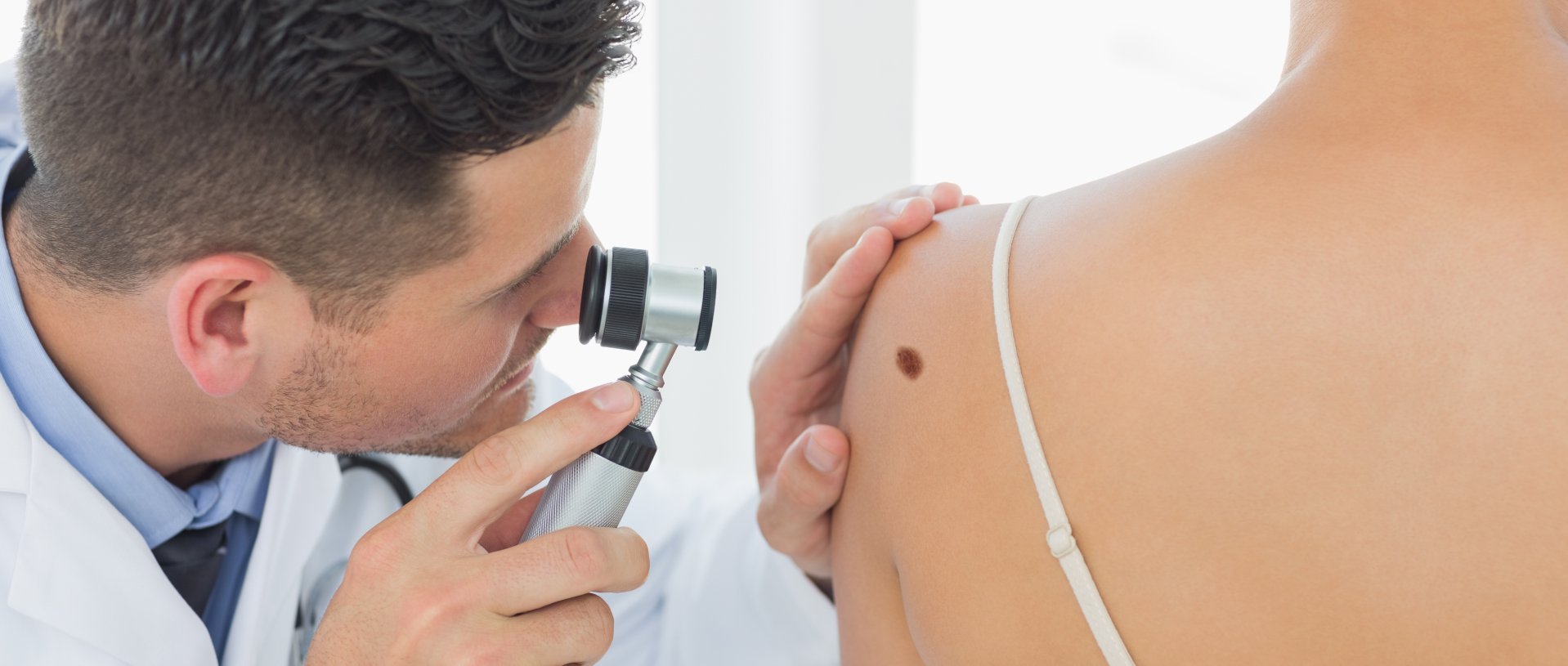 male doctor examining mole on back of woman