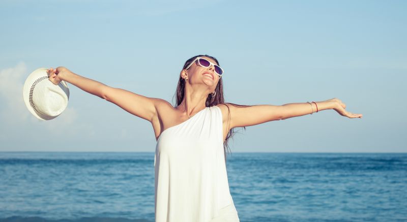 Mujer feliz después del levantamiento de antebrazo y brazo superior, parada en la playa con los brazos estirados