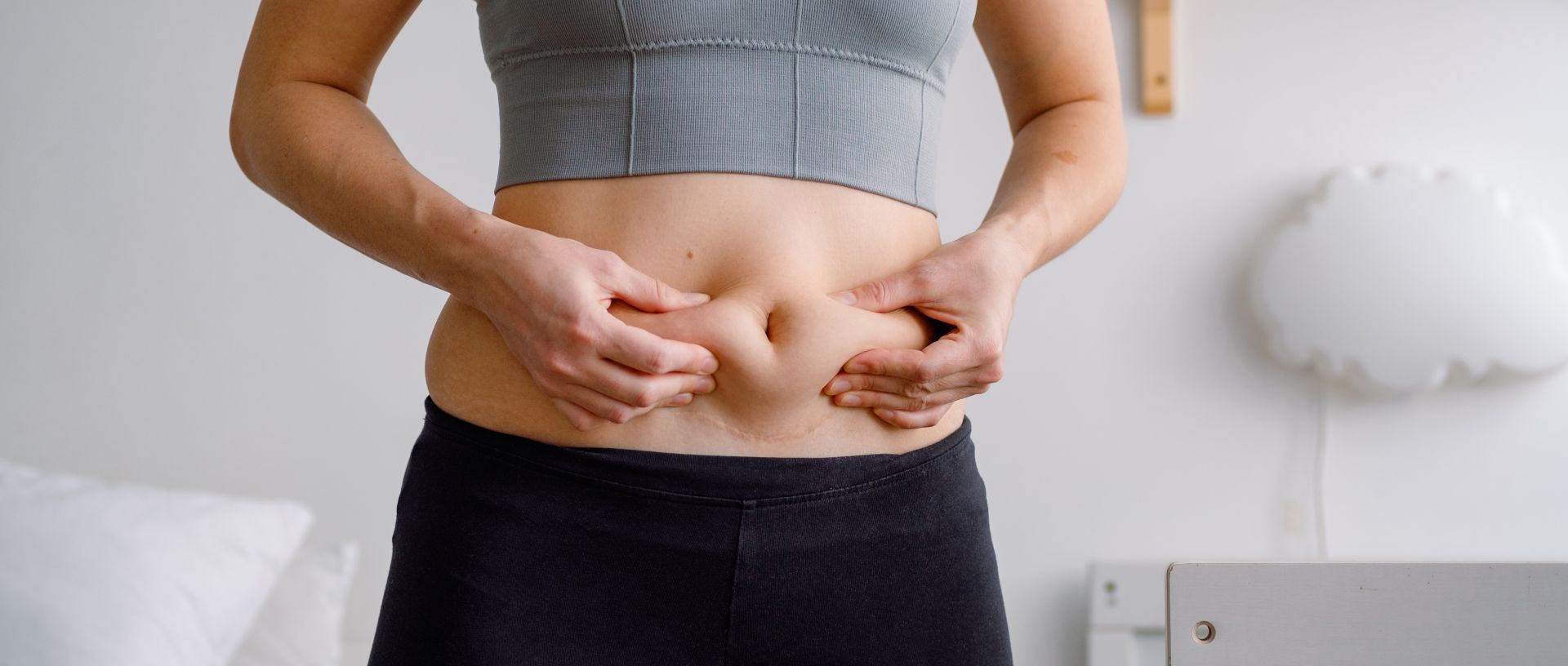 Concerned woman with a visible C-section scar wearing sports clothes and squeezing stretched skin on her tummy