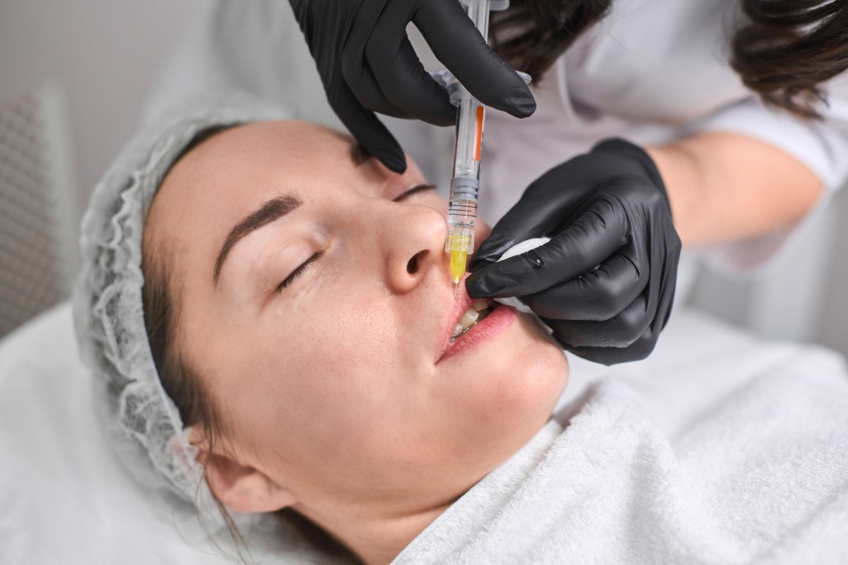 Professional administers dermal filler injection to relaxed young woman.