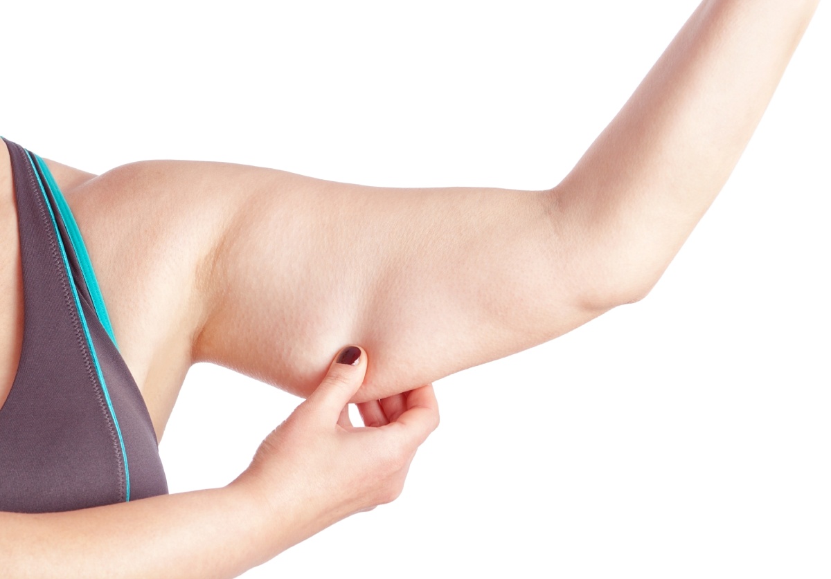 Person pinching loose skin on upper arm, highlighting excess or sagging skin. Arm is extended and background is white.